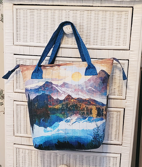 This quilted tote bag kit uses a panel featuring mountains with an option of blue, turquoise/rust or brown handles and lining. Designed by Kelly Mattson, this quilted tote measures approximately 14” wide x 14” tall x 6” deep. The kit includes all the required fabric, pattern, zipper and Frixion pen. You'll need to provide Bosal In-R-Form single sided fusible cut to 19” x 37”.