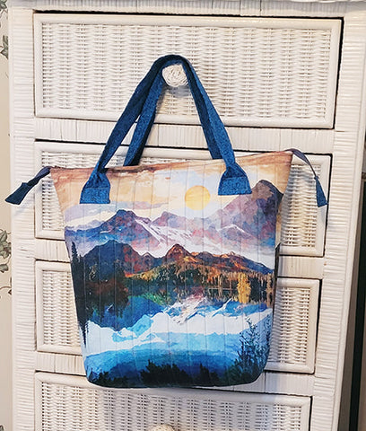 This quilted tote bag kit uses a panel featuring mountains with an option of blue, turquoise/rust or brown handles and lining. Designed by Kelly Mattson, this quilted tote measures approximately 14” wide x 14” tall x 6” deep. The kit includes all the required fabric, pattern, zipper and Frixion pen. You'll need to provide Bosal In-R-Form single sided fusible cut to 19” x 37”.
