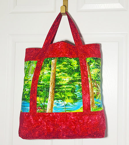 Red tote bag with a nature scene print hanging on a white door back
