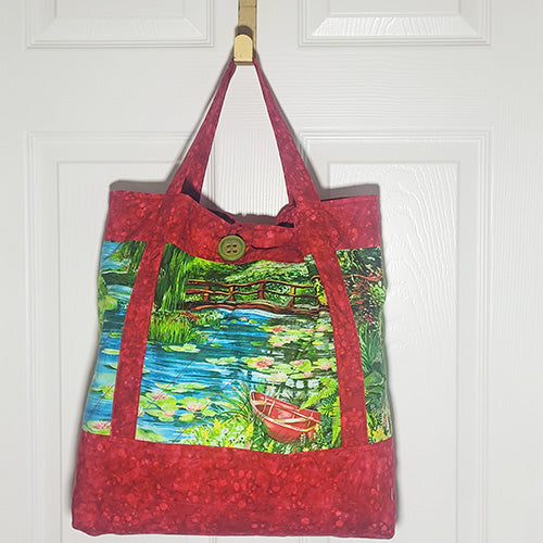 This quilted cotton tote features a red boat in a serene pond along with red handles and accents.  Front