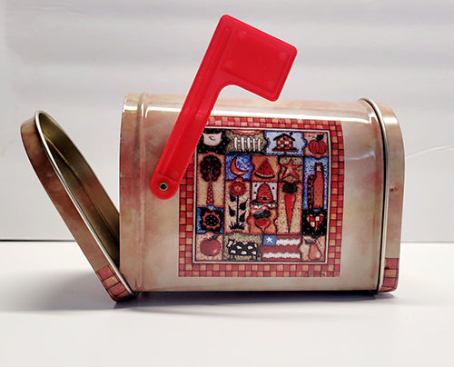 Decorative tin mailbox with a red flag and quilt design on a white background