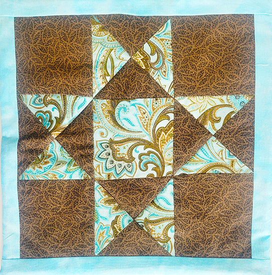Quilt block with brown and turquoise star pattern on a light blue background