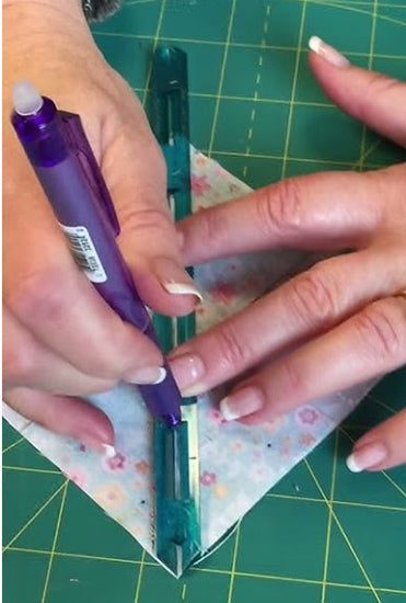Person using a blue tool on a piece of fabric with floral design on a green cutting mat.