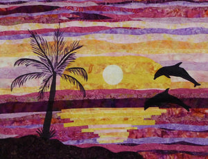 Dancing Dolphins quilt shows a silhouette of a palm tree and two dolphins jumping out of the water in front of a setting sun. Available at Colorado Creations Quilting
