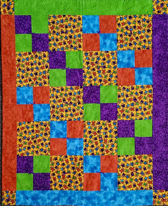 This handmade quilt features blocks with brightly-colored teddy bears on a yellow background alternating with blocks in blues, greens, oranges and purple. Designed by Jackie Vujcich, this quilt measures approximately 39"W x 47"L.  