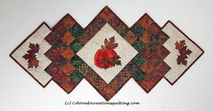 Fall Harvest table runner has a center square set on point with an appliques pumpkin on it.  Additional borders and applique maple leaves surround the center.