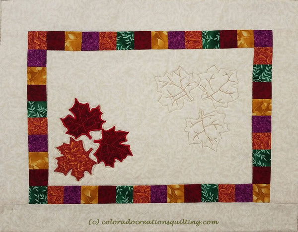 Fall Leaves quilted placemat has a cream center square with three applique maple leaves on it.  Additional small squares border and another cream border surround the center.