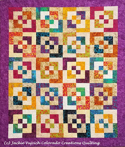Expolding Blocks quilt shows broken square multi-olored blocks on a light background with a violet border available at Colorado Creations Quilting