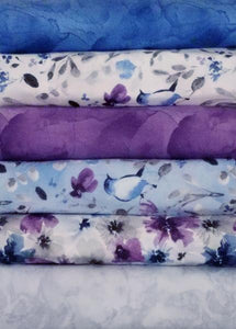 A 6-Pack is six coordinated half-yard pieces of fabric. This particular kit is called Awakenings. It includes various shades of blue, purple and gray fabric with bird and flower images.