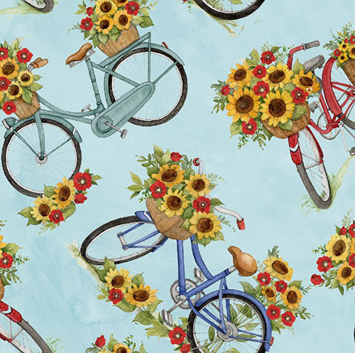This cotton fabric features bikes with baskets filled with bunches of sunflowers on a light blue background.