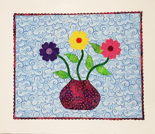 This darling little one of a kind art quilt features a flower pot with three brightly colored daisies on a blue background with a unique edging. Available at Colorado Creations Quilting