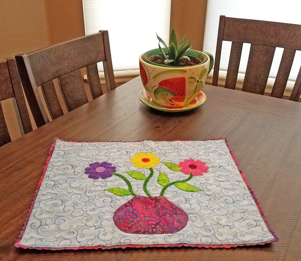 This darling little one of a kind art quilt features a flower pot with three brightly colored daisies on a blue background with a unique edging. Available at Colorado Creations Quilting